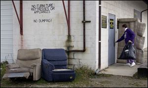 LuAnn Nagel carries a bag of clothing into the Sandusky County Share & Care past broken-down furniture left outside in deference to the sign overhead. Disposing of such items `costs us money we could use to help needy families,' she says.