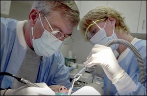 Bowling Green dentist Dr. Jack Whittaker treats one of his patients as dental assistant Aimee Fox helps out.