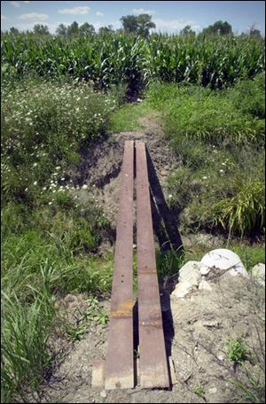 Metal strips form a makeshift bridge across a creek before a dusty path leads through the corn stalks to the cemetery.