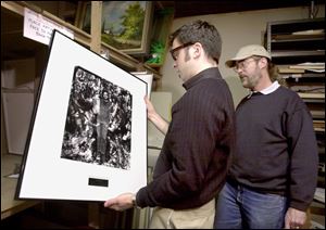 Marc Folk, left, art in public places coordinator, and Bill Chapin look over some of the art stored at Mr. Chapin's frame shop on Adams Street.