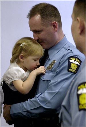 Samantha Bombrys plays withthe badge worn by her father, Matthew, after his promotion to sergeant yesterday at the Safety Building.
