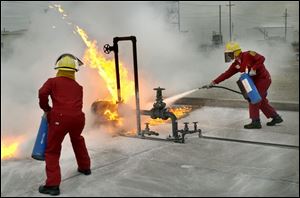 CTY May 11, 2004 - Steve Asmus, left, of the Anderson's in Maumee, and Ray Hixson of the West Alexandria, O. Fire Dept. and Rohm & Haas, an industrial chemical company in West Alexandria, learn to put out a gasoline fire with a dry chemical agent on equipment at the BP Oil Refinery Fire Field in Oregon.  They are participants in the State Fire School which is conducting some of it's training at the refinery.  Blade photo by Dave Zapotosky   CTY fire11p