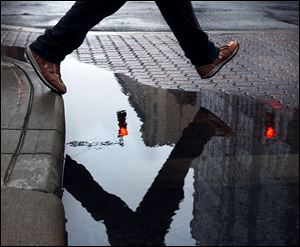 A pedestrian hops a puddle at the corner of North Huron Street and Madison Avenue. That puddle of water should turn into a sheet of ice tonight as the temperature dips into the 20s. 