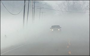 A vehicle makes its way down Salisbury Road in Monclova Township through a thick blanket of fog.