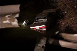 CTY accident15p 1 A diver hooks chains to a car that went through a guard rail , in foreground, on Alexis Road Tuesday, 03/15/05, in Toledo, O. The car crashed into a creek. The Blade/Jeremy Wadsworth