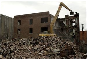 An excavator is used to demolish an apartment building at 2107 Putnam St. that has been vacant since 1957. It had attracted vagrants and drug users to the neighborhood.