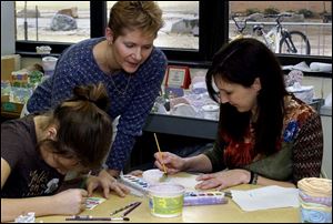 Teacher Andrea Baker oversees painting on a mosaic tile by Cortney Crable and her mother, Cherise Crable. 
