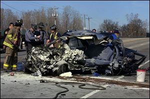 State troopers and firefighters examine the remnants of a burned car on Airport Highway after it crashed with a tractor-trailer rig yesterday afternoon, killing the car's driver.
