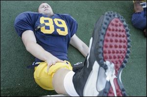 While his teammates scrimmage, Andrew Clarke can only watch and stretch.
