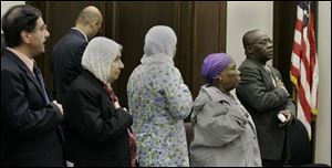 New citizens recite the Pledge of Allegiance as part of the naturalization ceremony yesterday at the federal courthouse. Judge James Carr serves as photographer for new citizen Teresa Neiswander, with her husband, Mike, and their children, from left, Sean, Sarah, and Sammy.