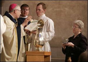 Bishop Leonard Blair consecrates the holy chrism in Rosary Cathedral while Sister Donna Jeanne Frey holds balsam that will give the oil its fragrance.
