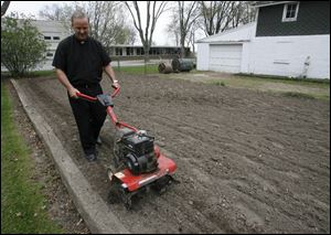 The Rev. Dennis Metzger of Holy Trinity Catholic Parish runs a tiller through his garden at the Assumption church.