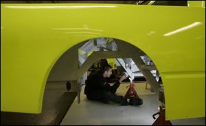 Seen through empty wheel wells, ThorSport fabricator Zac Teusher installs a lead box cover under a truck.