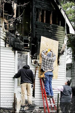City of Toledo workers Chris O'Larry, left and Stan Harris board up the house at 814 St. John Ave. where four people died in a fire. A suspect was charged in their deaths yesterday.