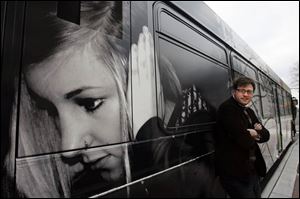 Tyler Fortney, a Bowling Green State University student from Medina, Ohio, stands by his artwork that graces this bus.