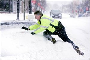 Police officer Dave Hartsel climbs onto a pile of snow to reach the top of a car in downtown Tiffin. Once there, he left a parking ticket as a reminder to the owner.
