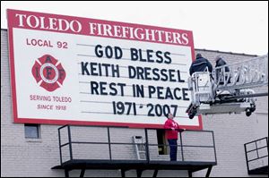 Fire union Local 92 s Rick Syroka thanks firefighters Oliver Harris and Roger Vorraber, in bucket, for helping with a memorial message to the slain detective on Local 92 s building downtown.
