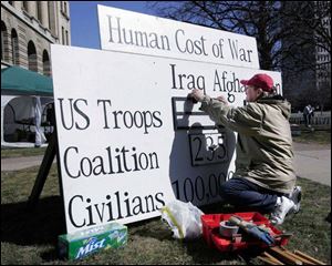 Stephen Masternak of Toledo, a Navy veteran and member of the Northwest Ohio Peace Coalition, erects a sign tallying war deaths.