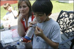 Carl Antrassian demonstrates what he must do to use his inhaler as his mom, Johanna, center, and brother Neil watch. Carl and his entire family are well-acquainted with his regimen of medication.