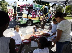 Some want to color during a Fun Bus stop at Nathan Hale School while one young man finds a Hula Hoop intriguing.