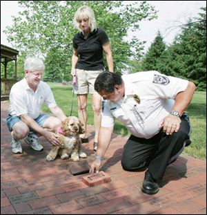 Bill Pilliod, his finacee, Cami Waller, and their dog, Mutley, watch Swanton Police Chief Homer Chapa install a memorial brick bearing Mutley's name into the sidewalk at Pilliod Park in Swanton. The brick for Mutley, who is walked in the park every day, features two hearts and two paw prints.
