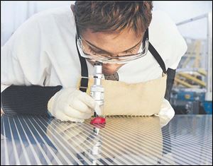 An employee of First Solar's Perrysburg Township plant uses a magnifier to examine the spacing of laser scribes on a solar panel.