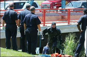 Toledo firefighters and members of the water-rescue team remove the body of a man from Swan
Creek in front of the Owens Corning headquarters downtown. A tour boat captain saw the body and called authorities, who pulled the body from the creek at 2:30 p.m. yesterday. 