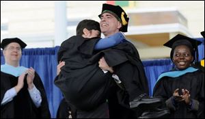To a rousing ovation, Randy Pausch, a computer science professor, carries his wife, Jai, to their seats after giving the charge to Carnegie Mellon graduates May 18 as he was dying of cancer.