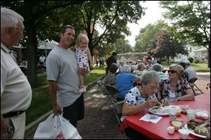 Landry Sheets holds his 19-month-old daughter, Emerson, at a chicken barbecue near the Pemberville Opera House and talks to Eileen Schuerman, seated left, and Inga Offerman, right. 