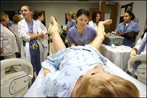 Dr. Lina Ea, center, an intern, delivers a baby by Noelle the simulator. Dr. Ashley DeWitt, left, and Dr. Alexandra Schmidt, back right, help supervise the  delivery  of the doll baby.