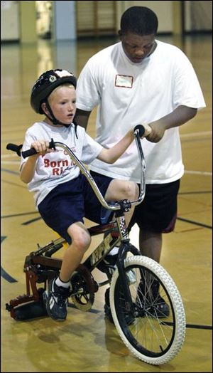 Daniel Rocker works with Jake Emch, 8, of Oregon as he practices on a bicycle with a roller instead of a back wheel. Such camps are planned for 53 U.S. and Canadian cities this year.