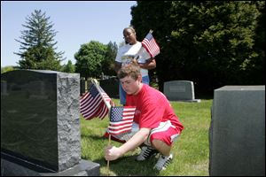 Chante Ruch, 17, kneels down to affix a flag to a grave at Toledo Memorial Park as Alisha Thompson, 16, holds the supply. Both Whitmer students are part of an annual drive to ensure at least 50,000 fallen Lucas County veterans are honored with a flag. 