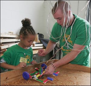 Clay High School alumnus Derek Partin assists Daijah Sartor, 8, with her car during the Robot Wars program.