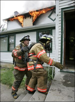 Sylvania Township firefighter Greg 'Jumbo' Wilcox, left, guides trustee Carol Contrada into the 'controlled-burn house.' Ms. Contrada had participated in exercises before, but this was her first experience with flames.
