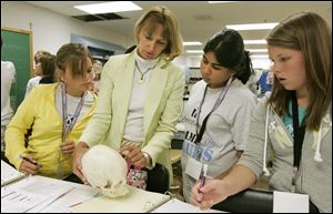 The Blade/Dave Zapotosky Barbara Stoos, assistant dean of sciences at Mercy College of Northwest Ohio, instructs students, from left, Allison Ahrens, 13, of Marblehead, Shailaa Kummar, 14, of Sylvania, and Maty Lehman, 13, of Rossford, on the fine points of determining the age and gender of a human skull.