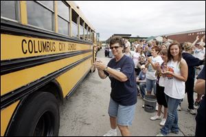 Judy Welland, a food service worker at Lake schools, center, joins volunteers in cheering the arrival of donated buses from Columbus City Schools to replace several damaged Lake vehicles.