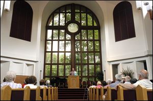 At First Seventh-day Adventist Church, the Rev. Mike Fortune speaks to the visitors as he stands before a 43-foot window that looks out on a lush patch of trees and Sylvania Avenue. 