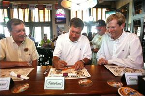 James Seney, left, former mayor of Sylvania, and Jon Stainbrook, right, Lucas County GOP chairman, watch John Kasich as the candidate for Ohio governor signs a hot dog bun at Packo's in the Park.