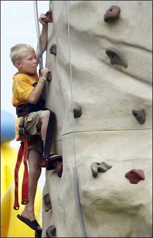 Harnessed for safety, 8-year-old Hunter Dillman grabs toe and hondholds as he tests his skills on a climbing wall at the Fun Fest.