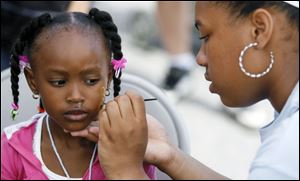 Talia Ulrich concentrates as she paints a design on the face of La'Nyah Foster, 3, during the Family Fun Fest.