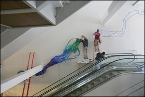 Workers begin the installation of the work, which is made from thousands of pieces of blue, green, and purple plastic.