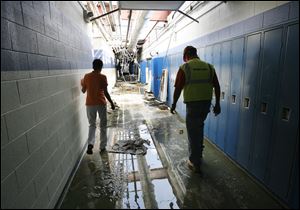 Lake Local Schools board member Margene Akenberger, left, and Joe Vancena of Rudolph/Libbe slosh down a hall at the damaged school. As they toured the building, they dodged puddles, heaps of debris, soggy insulation, and broken wires and pipes.  The sky is visible through the library door ahead of them.