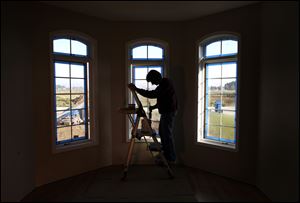 Carolyn Booth is framed in the window bay as she paints the dining room of a house under construction on Tournament Drive in Monclova Township.