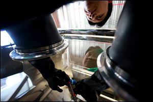 Graduate student Rhet De Guzman, 26, uses a voltage tester on a prototype lithium cell in an oxygen-free box at Wayne State University in Detroit. He says he can see that the auto industry is now ‘solid.'