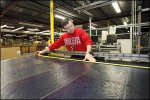 Bill Gaston, an employee of Xunlight Corporation, measures a piece of flexible solar panel at the Toledo office.