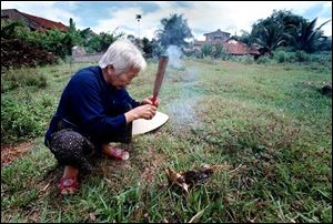 Tam Hau lights incense before kneeling in prayer at the grave of her uncle, Dao Hue, who was killed by a Tiger Force officer.