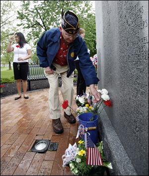 Korean War veteran Joe Stockner of Perrysburg places a flower by a World War II memorial at Waite High School after its program. 