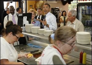 Mr. Obama ordered a chili dog, french fries, and a bowl of chili during the visit to Rudy’s as Mayor Mike Bell and U.S. Rep. Marcy Kaptur wait their turn. At right is Rudy’s co-owner Harry Dionyssiou.