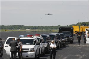 Air Force One approaches Toledo Express Airport as law enforcement, their vehicles, support vans, and limousines await the President.