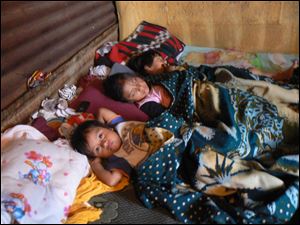 Romelia Suret worries, as most mothers do, about her children. Mrs. Suret's house of tin is in a ghetto with alleys through which runs an open sewer and where standing water means a breeding ground for malaria-carrying mosquitoes. Her three children lie listless in bed. Although government doctors say nothing is wrong with them, private physicians say Jennifer, center, has E. coli.